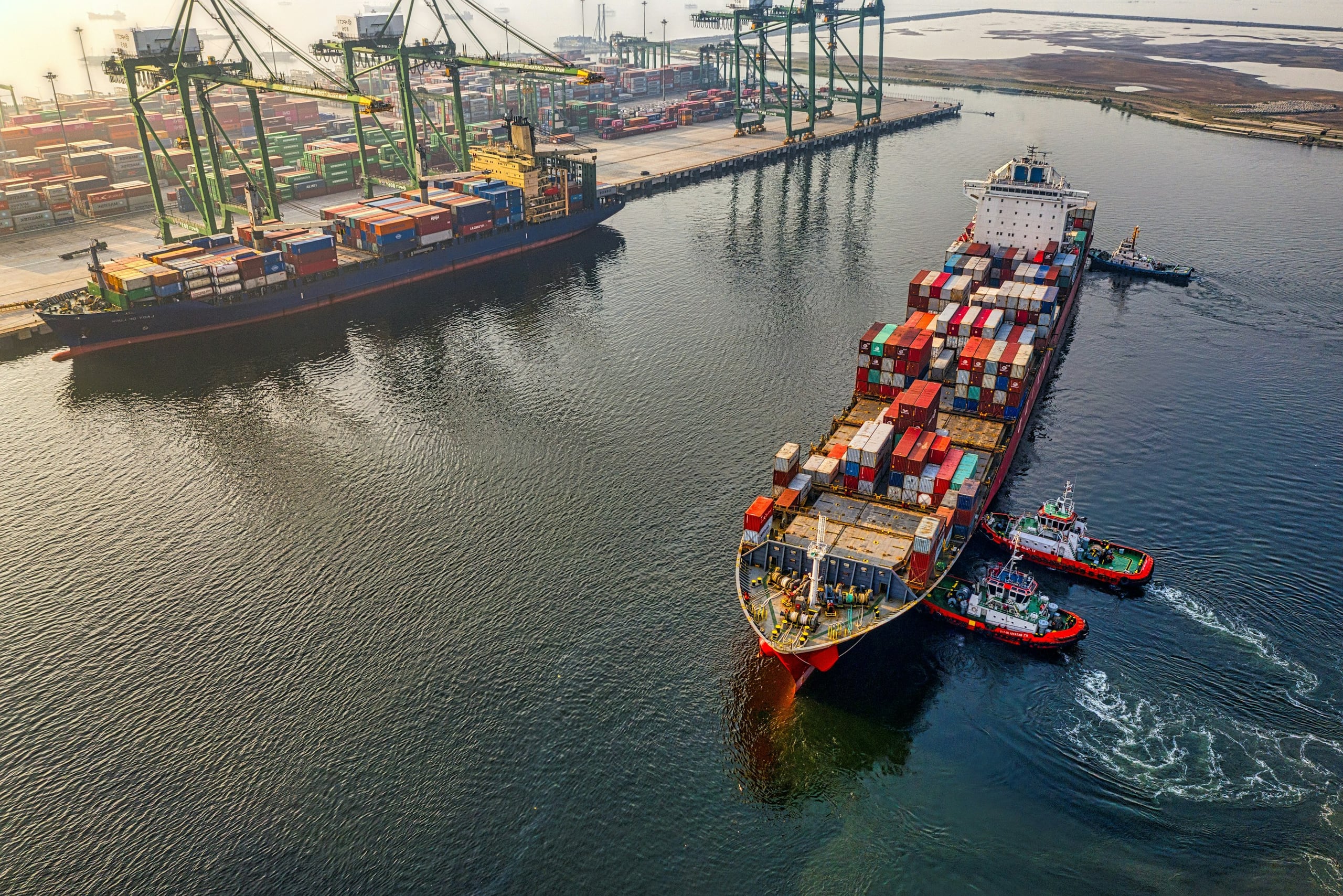 Container ship guided into port by tugboats